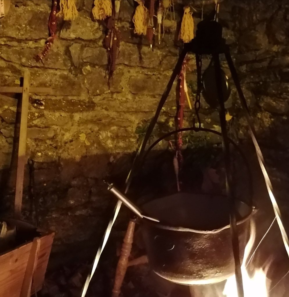 A Cauldron over a fire, a brick wall behind it.