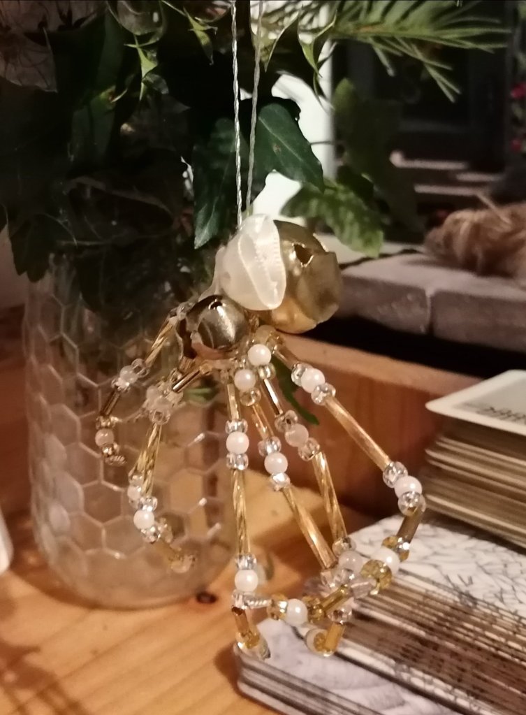 A spider decoration made of gold and silver beads hanging from a piece of holly.