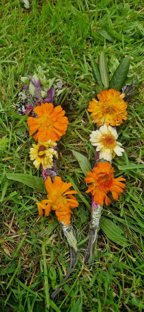 bundles of flowers and herbs tied together with colourful string to be burned for use in smoke cleansing rituals. orange calendula's laying on green grass.